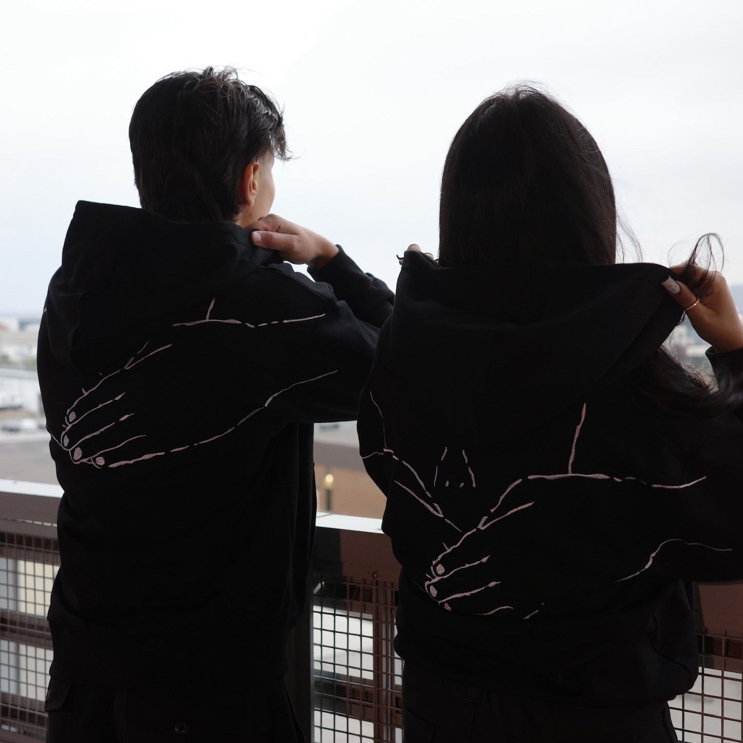 Two people in dark hooded robes standing close together by a window with a snowy landscape.
