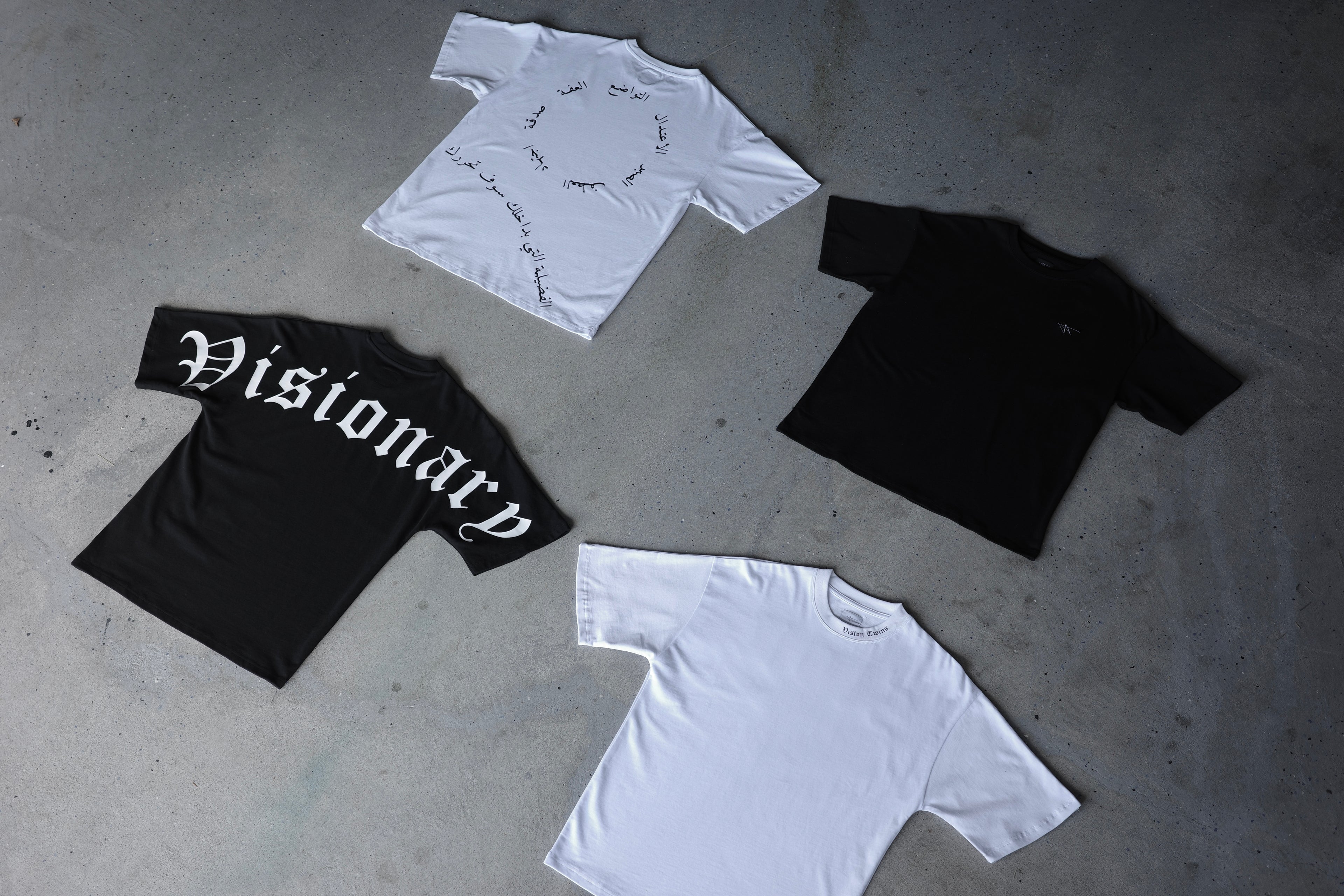 Four t-shirts in black and white on a concrete floor with 'Visionary' text.