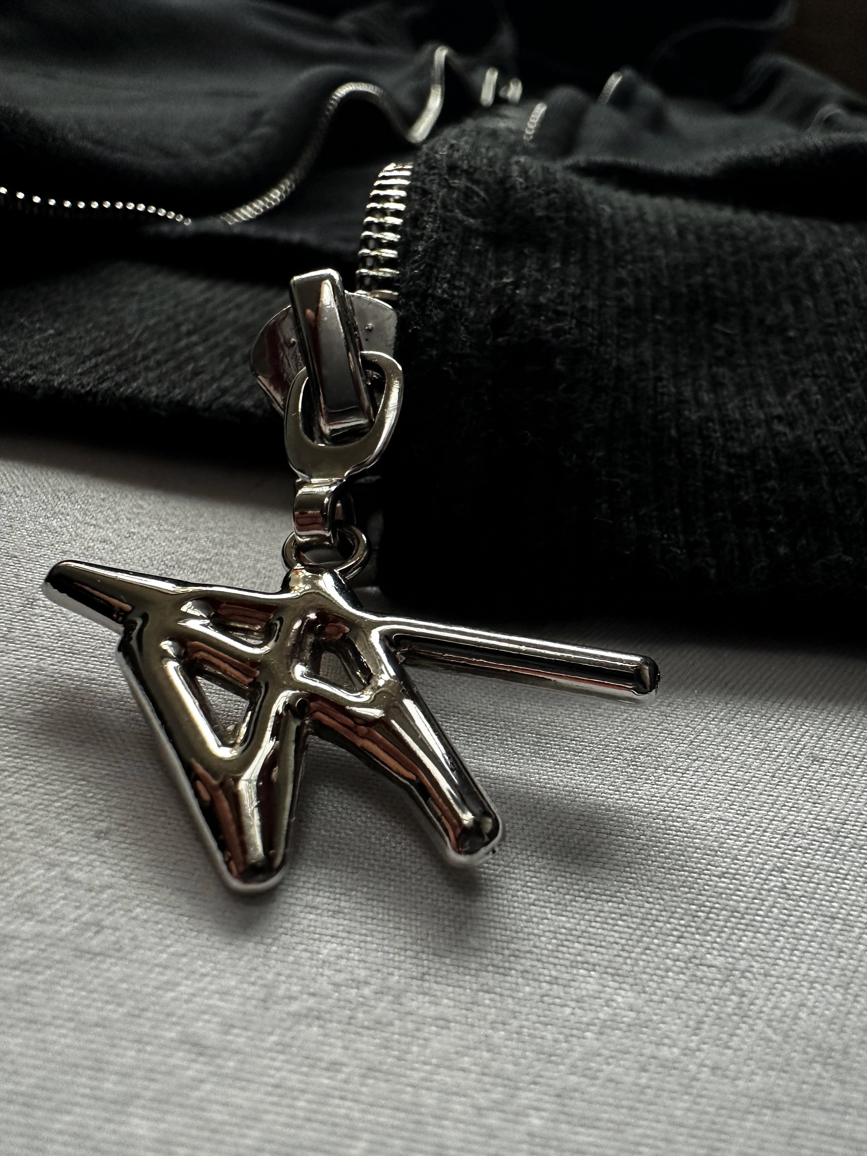 Metallic pendant on a chain against a black garment background