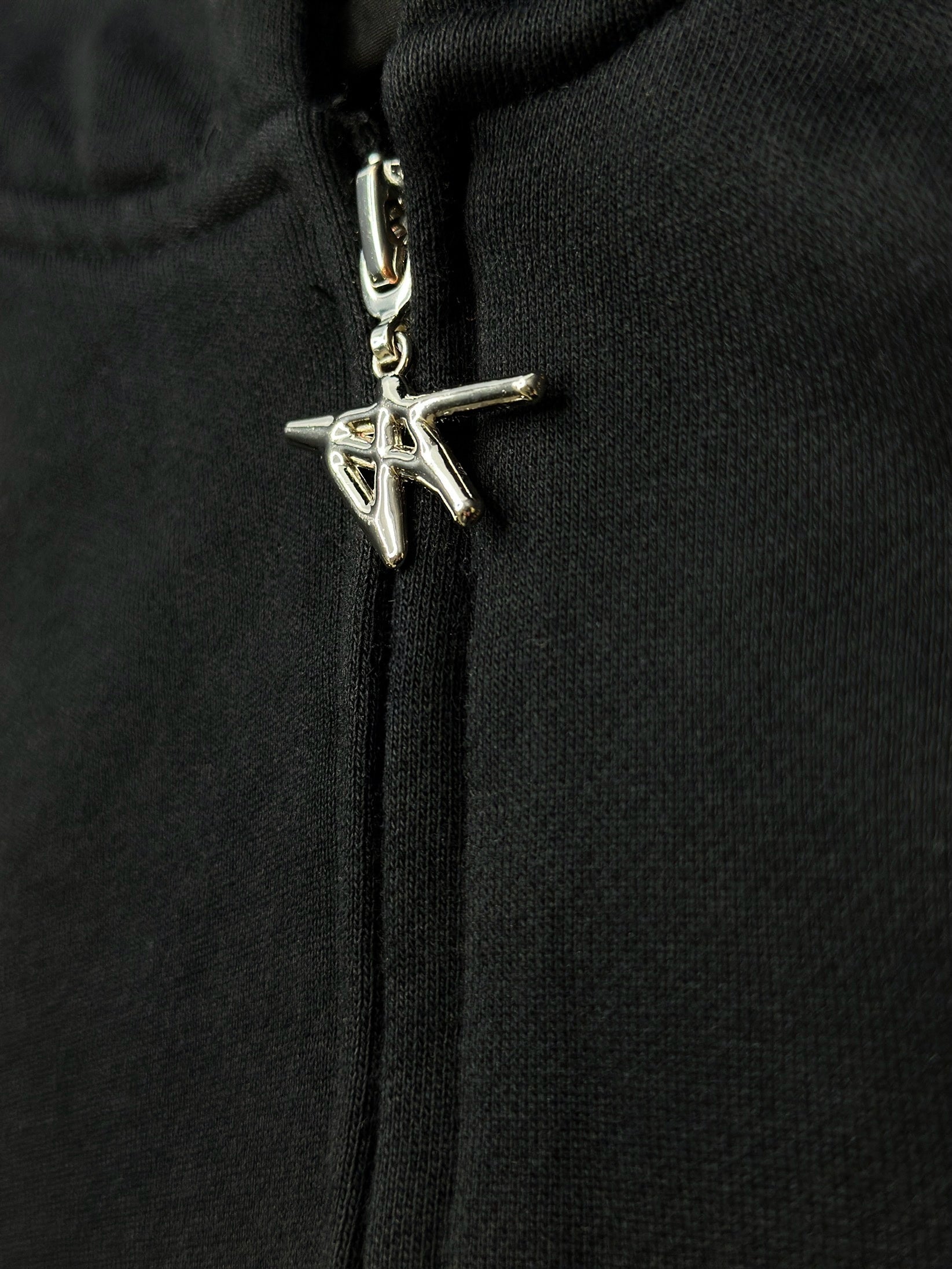 Close-up of a black hoodie with a silver zipper pull featuring a logo.